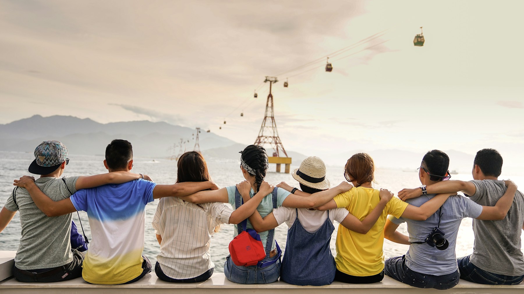 A row of students sitting with their arms around each other, looking out at the sea
